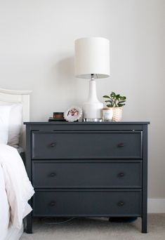 a black dresser sitting next to a bed with white sheets and pillows on top of it