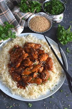 a white plate topped with rice covered in meat and sauce next to bowls of vegetables