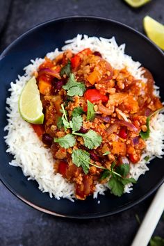 a black plate topped with rice and meat covered in cilantro next to a lime wedge