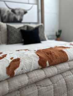 a cow print blanket on top of a bed in a room with white walls and pillows