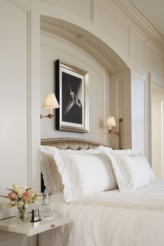 a bed with white linens and pillows in a bedroom next to a painting on the wall