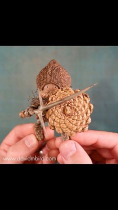 a person holding a tiny pine cone with a cross on it's end,