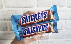 a hand holding two snickkers crisper bars in front of a brick wall