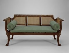 an old wooden bench with green cushions and caned back rests against a gray background