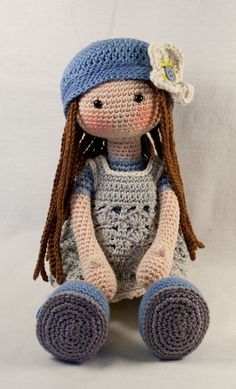 a crocheted doll is sitting on the floor wearing a blue hat and dress