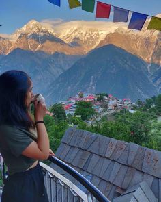 a woman standing on top of a balcony talking on a cell phone with mountains in the background