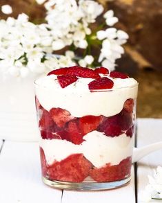 a dessert with strawberries and whipped cream in a glass jar on a white table