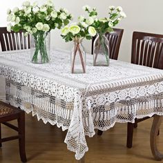 two vases with white flowers sit on a table in front of some wooden chairs