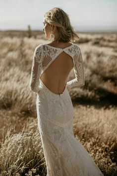 a woman in a wedding dress is standing in the grass with her back to the camera