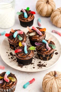 chocolate cupcakes decorated with candy worms and candies on a plate next to pumpkins