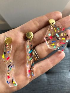 a hand holding three different colored earrings in it's left hand, with confetti and sprinkles on them