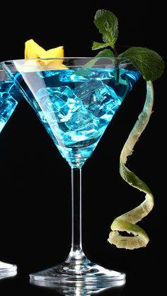 two glasses filled with blue liquid and garnished with green leaves