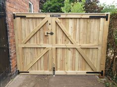 a large wooden gate with black hardware on the top and bottom bars, in front of a brick building