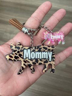 a hand holding a keychain that has a cow on it and the word mommy written in leopard print