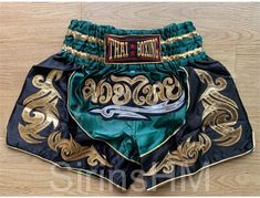 the thai boxing shorts with gold and green trimmings are displayed on a wooden floor