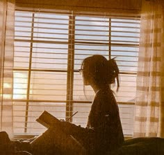 the silhouette of a child sitting on a bed in front of a window with blinds