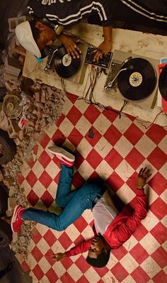 a man laying on top of a red and white checkered floor next to a record player