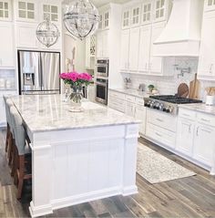 a large kitchen with white cabinets and marble counter tops, an island in the middle