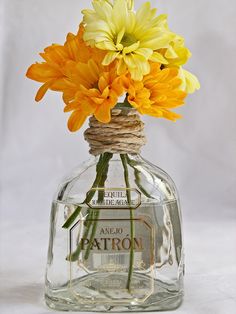 yellow flowers in a clear glass bottle with twine on the top that says patron