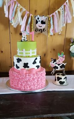 a three tiered cake is decorated with pink, green and white icing on a table in front of a wooden wall