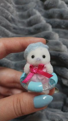 a hand holding a tiny stuffed animal in a glass bowl with a pink ribbon around it