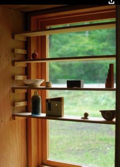 a window with shelves and bowls in front of it, next to a grassy field