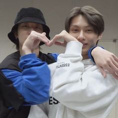 two young men standing next to each other in front of a white wall and one is making the v sign with his hand