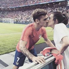 a man and woman kissing on the sidelines at a soccer game in front of an audience