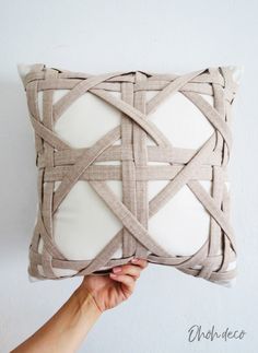 someone is holding up a pillow made out of woven fabric and white linen with a knoted design on the front