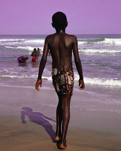 a young boy walking on the beach towards the ocean with other people swimming in the water