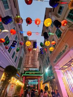 many colorful lights hanging from the ceiling in a shopping area with people walking down the street