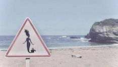 a warning sign on the beach with a rock in the background