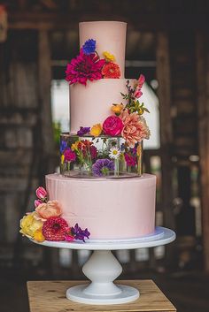 a three tiered cake with pink frosting and colorful flowers