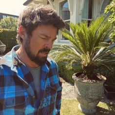 a man standing in front of a house next to a potted plant and looking at his cell phone