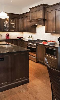 a large kitchen with wooden floors and dark wood cabinets, stainless steel appliances and an island