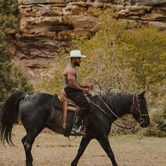 a man riding on the back of a black horse next to a rocky mountain side