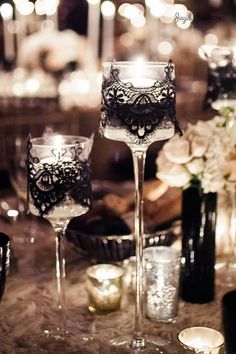 two wine glasses sitting on top of a table next to candles and vases filled with flowers