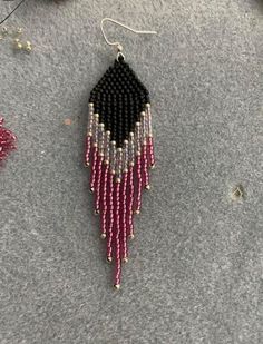 a pair of pink and black beaded earrings sitting on top of a gray surface