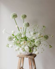 a wooden stool holding a vase with white flowers on the top and green stems in it