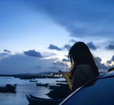 a woman is looking at her cell phone while sitting on the hood of a car