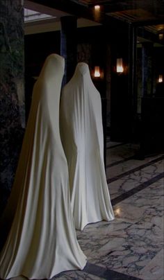 two white cloth covered mannequins are standing in the middle of a marble floor