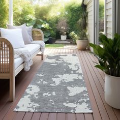 a porch with a couch and rug on the floor next to a potted plant