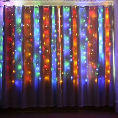 colorful lights are shining on the curtains in front of a window with white walls and wooden floors