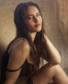 a woman with long hair sitting on the floor in front of a wall and looking at the camera