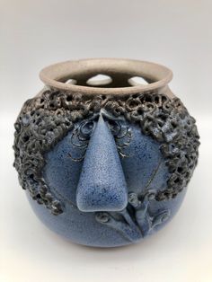 a blue vase with a face on the front and sides, sitting on a white surface