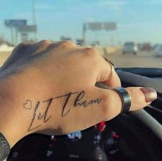 a person's hand holding the steering wheel of a car with a tattoo on it