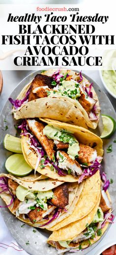 fish tacos with avocado and cream sauce on a plate next to lime wedges