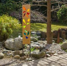 a wooden sign sitting next to a tree on top of a rock covered ground in a garden