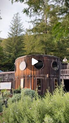 a round wooden structure in the middle of some trees and bushes with two circular windows