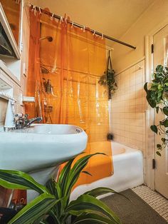 an orange shower curtain in a bathroom next to a sink and bathtub with plants